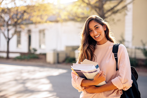 Beautiful young woman with backpack and books outdoors. College student carrying lots of books in college campus.