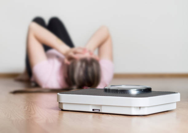 Weight loss fail concept. Scale and depressed, frustrated and sad woman lying on floor holding head and covering face with hands. Weight loss fail and depression low body fat stock pictures, royalty-free photos & images