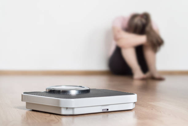 il concetto di perdita di peso fallisce. scala e donna depressa, frustrata e triste seduta sul pavimento che tiene la testa e le braccia in ginocchio. - emaciated weight scale dieting overweight foto e immagini stock