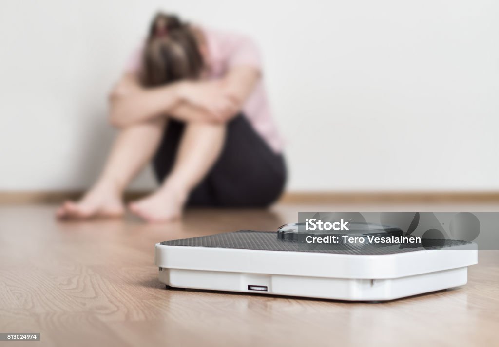 Concepto de error de pérdida de peso. Escala y deprimida, frustrada y triste mujer sentada en el piso sosteniendo la cabeza y los brazos en las rodillas. - Foto de stock de Régimen alimenticio libre de derechos