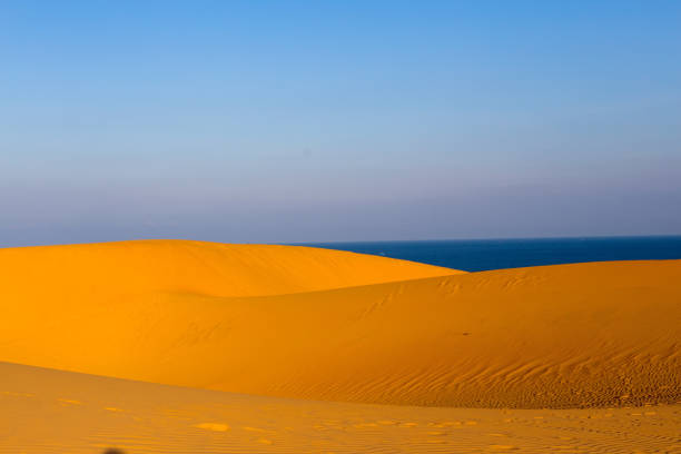 Yellow sandy wavy dunes with blue sea at background. Nobody. Nature landscape.