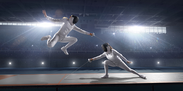 Fencing competitive duel. Female fencer fight on big professional stage. They are wearing an unbranded fencing suit.