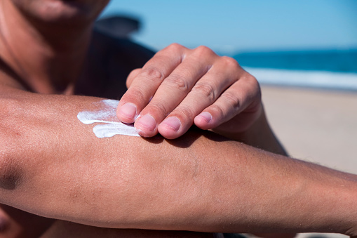 closeup of a young caucasian man on the beach man applying sunscreen to his arm