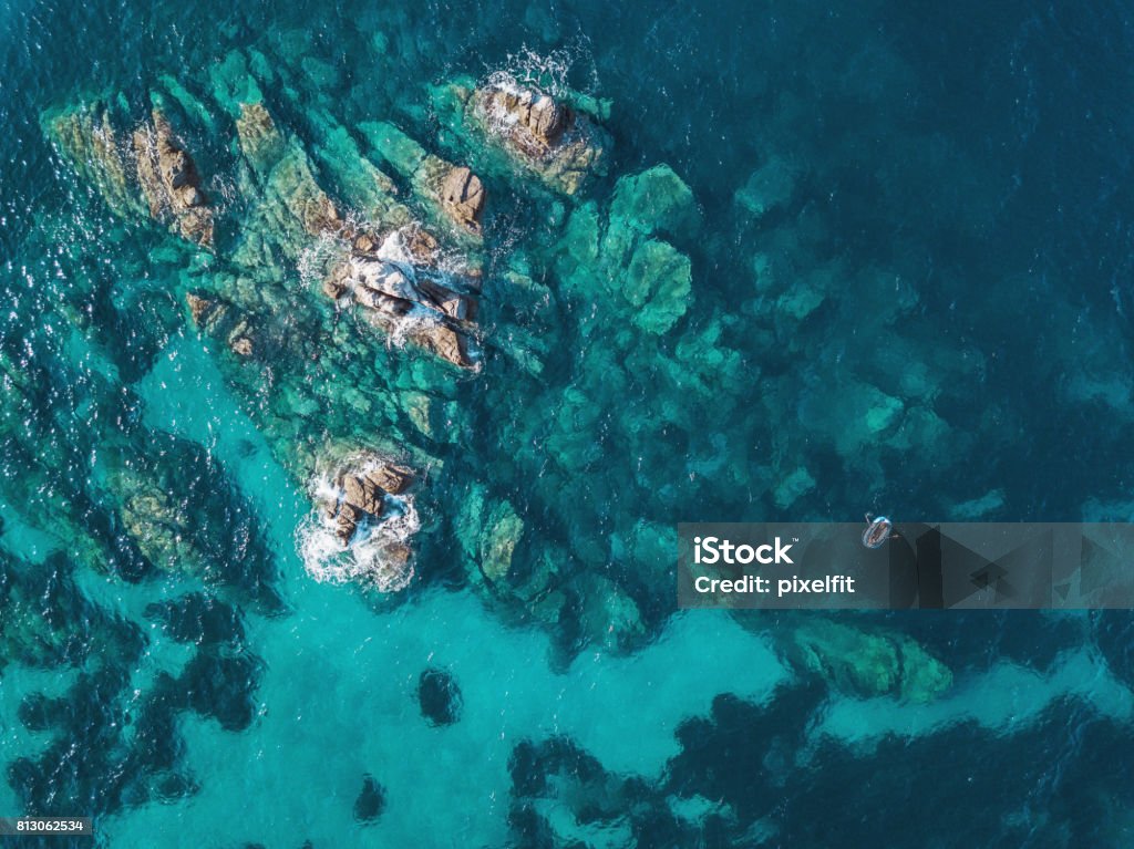 Lonely boat near reefs Aerial view of blue sea, rocks and a small boat Sea Stock Photo