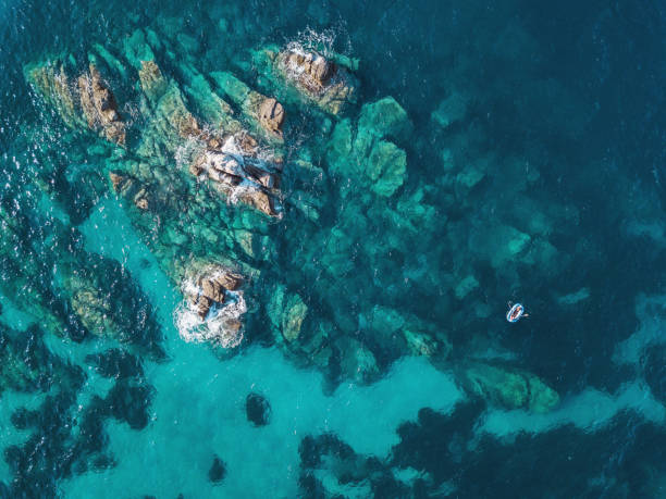 Lonely boat near reefs Aerial view of blue sea, rocks and a small boat turquoise ocean stock pictures, royalty-free photos & images