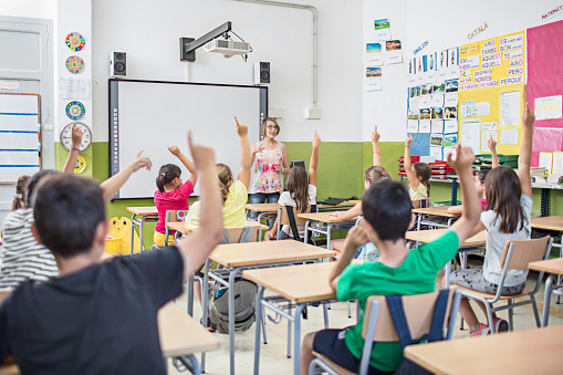 School kids in classroom raising hands wanting to answer a question.