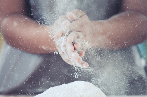 Woman hand prepare bread dough clapping and sprinkling white flour on dough for baking cookies in the kitchen in vintage color tone