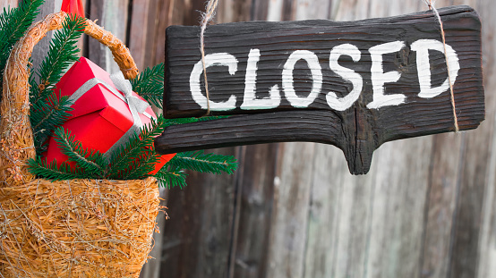 Wood sign 'Closed' with christmas decoration hanging over grey barn wall