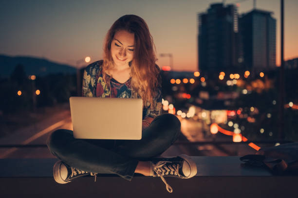adolescente con ordenador por la noche contra el horizonte urbano - travel red vacations outdoors fotografías e imágenes de stock