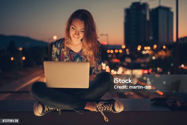 Teenage Girl Using Laptop By Night Against The Urban Skyline Stock Photo - Download Image Now