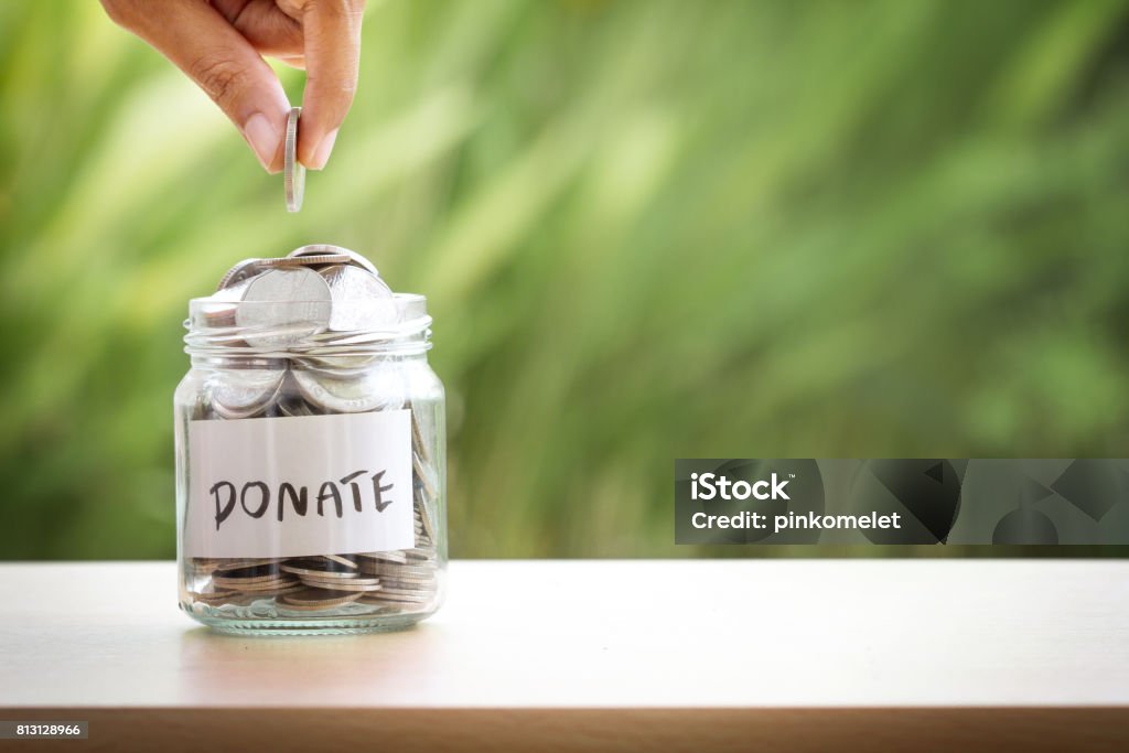 Hand putting Coins in glass jar for giving and donation concept Charitable Donation Stock Photo