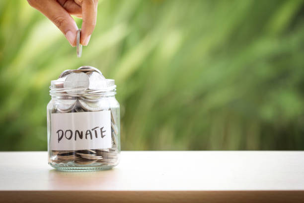 Hand putting Coins in glass jar for giving and donation concept stock photo