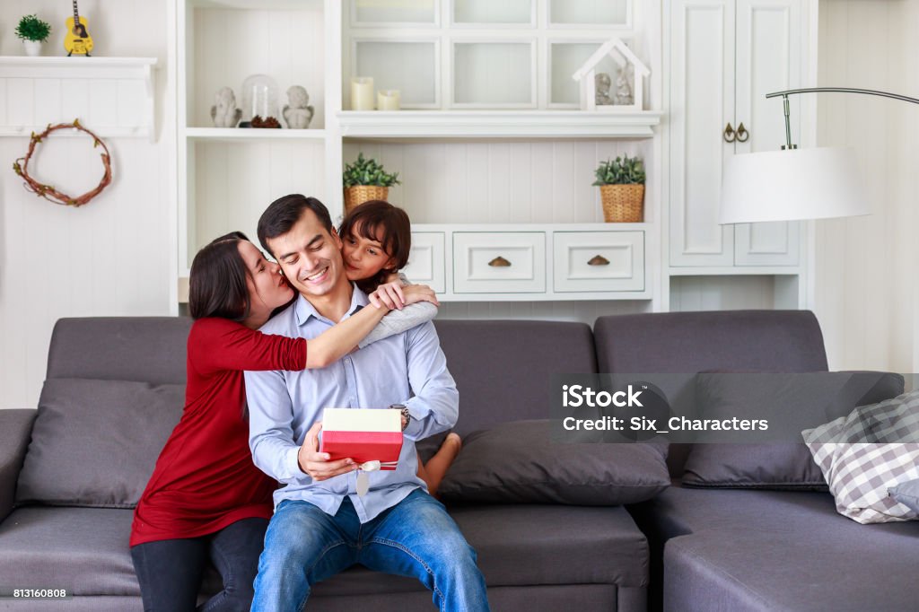 Tochter und Mutter überraschend Vater mit Geschenk zu Hause im Wohnzimmer, Mutter mit Kindern feiern Vatertag - Lizenzfrei Geschenk Stock-Foto