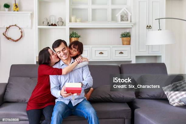 Daughter And Mother Surprising Father With Gift At Home In The Living Room Mother With Kids Celebrating Fathers Day Stock Photo - Download Image Now
