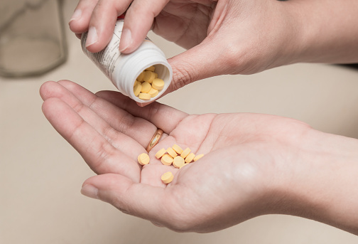 Woman holding medicines bottle and pouring some pills on another hand for treatment medication