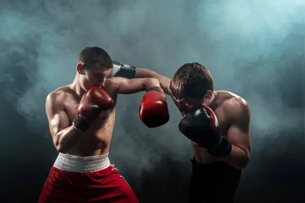Two professional boxer boxing on black smoky studio background.