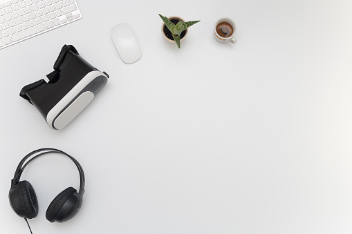 Vista superior del escritorio de trabajo. Escritorio multimedia con gafas de realidad virtual, Headphones, teclado, ratón, planta y una taza de café photo