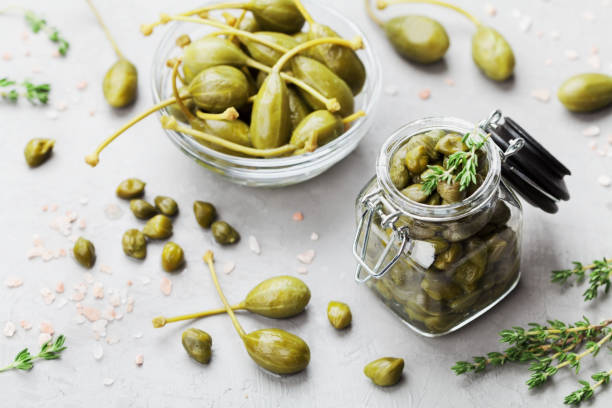 istock Mixed capers in jar and bowl on gray kitchen table. 813195860
