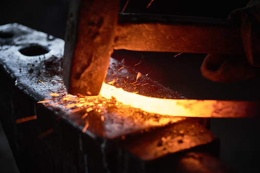 Close-up of blacksmith hitting hot metal with hammer on anvil