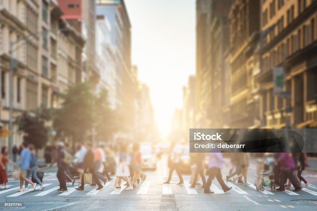 Grupo anónimo de personas caminando a través de un cruce peatonal en una calle de la ciudad de Nueva York con una luz brillante al atardecer brillando en el fondo - Foto de stock de Personas libre de derechos