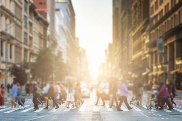 grupo anónimo de personas caminando a través de un cruce peatonal en una calle de la ciudad de nueva york con una luz brillante al atardecer brillando en el fondo - dusk people manhattan new york city fotografías e imágenes de stock