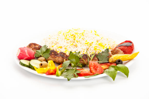 Low angle view studio shot of grilled lamb kebab koobideh with herbs and vegetables in the front and a serving portion of rice in the back of the plate. Food concept for traditional Iranian cuisine.