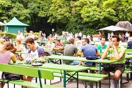 Munich, Germany - July 09, 2017: A lot of people sitting at the wooden tables and enjoying the sunny weather. They are drinking Beer and eating traditional Bavarian meals. The Englischer Garten is a large public park in the centre of Munich, Bavaria, stretching from the city centre to the northeastern city limits. With 7,000 seats, the beer garden at the Chinesischer Turm in the Englisher Garten is the second largest in Munich.