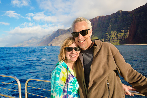 Tourist couple enjoying the scenic view on a Cruise Ship Tour Boar at the Na Pali Coast of the Kauai Island in Hawaii, USA. They are a Caucasian adult couple enjoining their vacation on a cruise ship tour.