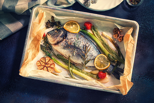 Freshly baked sea bream fish with lemon,herbs,vegetables and spices in a baking sheet