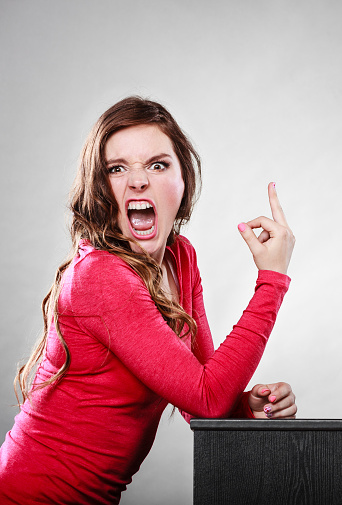 Angry furious girl showing middle finger gesture on gray.