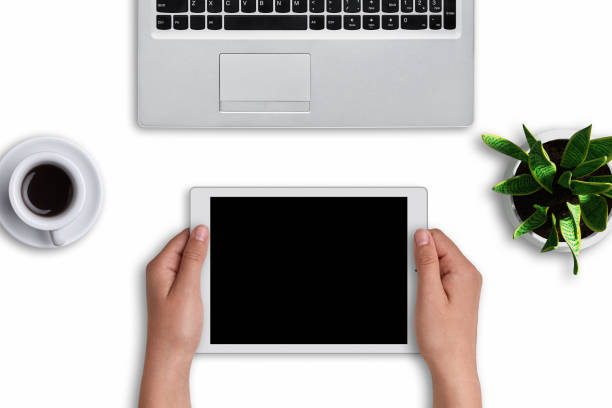 istock Woman`s hands holding modern tablet with blank screen over white background. Modern devices: tablet and laptop computer on white surface with cup of coffee and flowerpot with flower. Office design 813343706