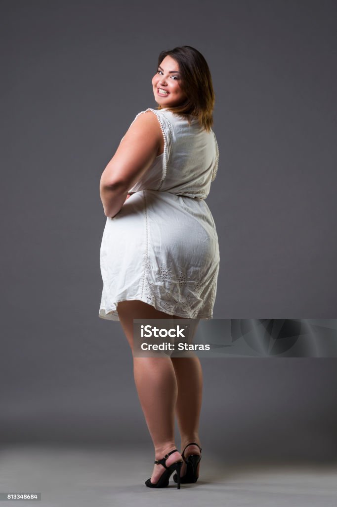 Happy plus size fashion model in casual clothes, fat woman on gray background, overweight female body Happy plus size fashion model in casual clothes, fat woman on gray background, overweight female body, full length portrait Buttocks Stock Photo