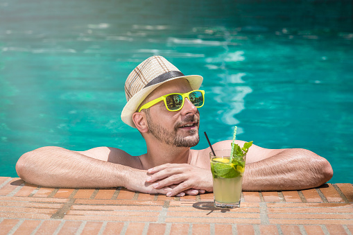 Man enjoying and relaxing in swimming pool with mojito cocktail