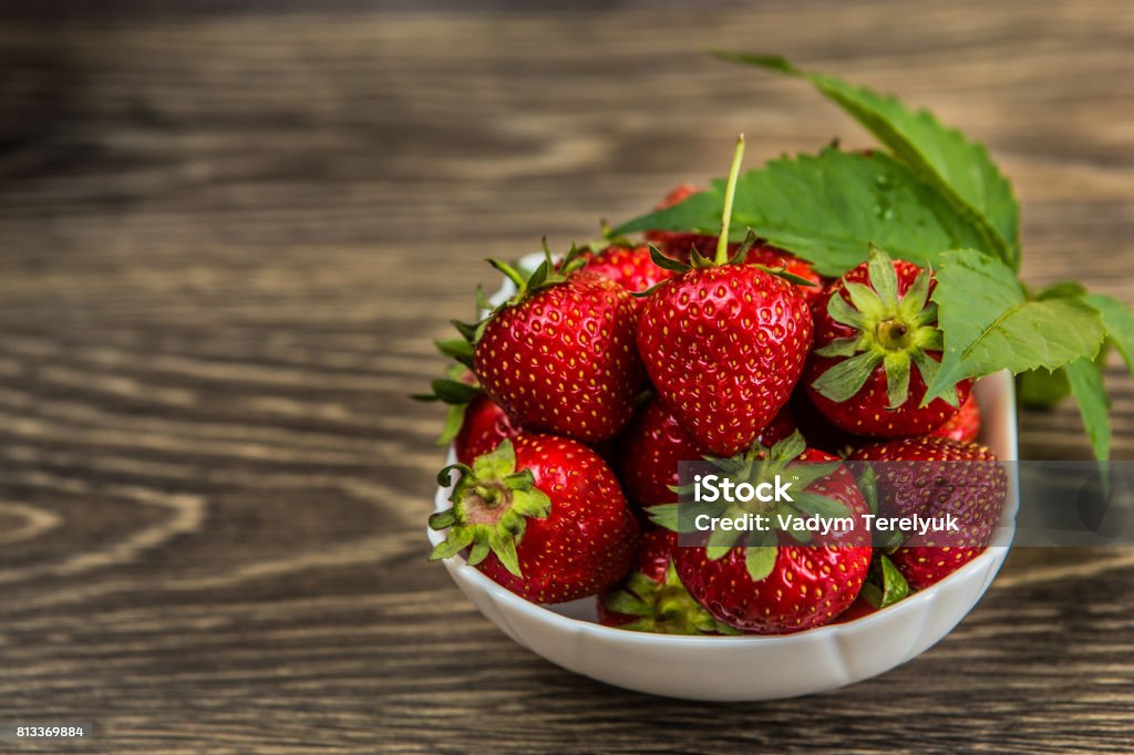 Small white china bowl filled with succulent juicy fresh ripe red strawberries on an old wooden textured table top. Fresh strawberries. strawberries on a wooden table Small white china bowl filled with succulent juicy fresh ripe red strawberries on an old wooden textured table top Agriculture Stock Photo