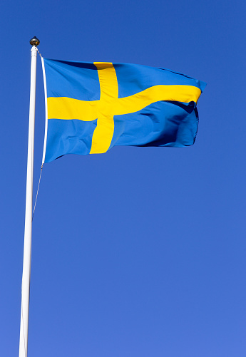 Swedish flag hoisted on a flagpole against a blue sky.