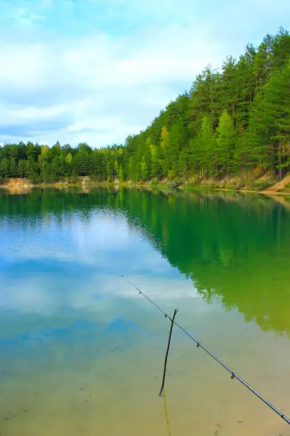 landscape with lake in the forest reflection on the water surface and fishing-rod