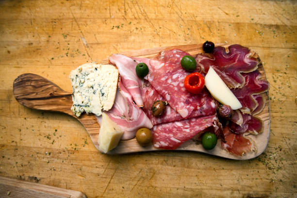 Delicious cold cuts of cured meat, ham or bacon, salami and prosciutto, parmesan, bleu and provolone  on a rustic cutting board.