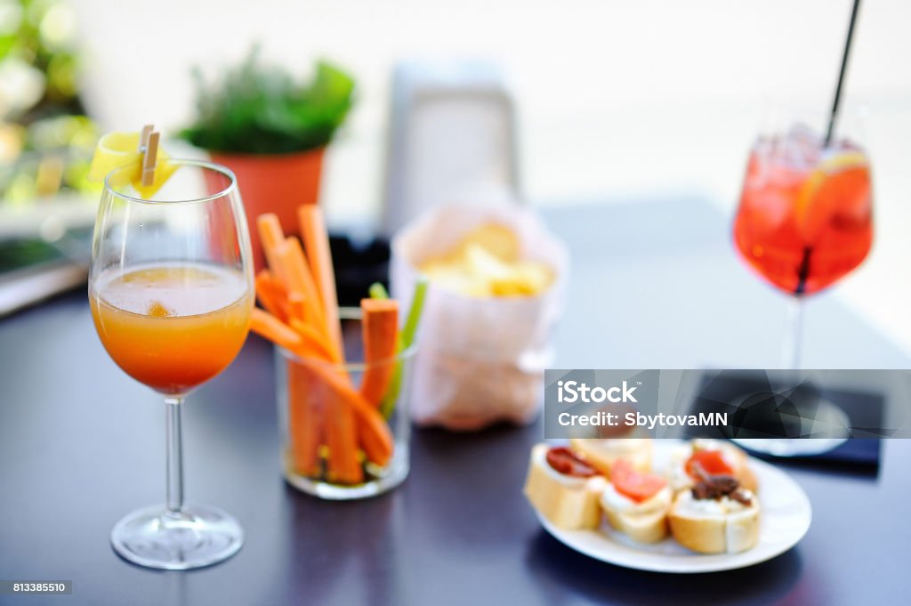 Italian aperitives/aperitif: two glasses of cocktail and appetizer platter on the table Italian aperitives/aperitif: two glasses of cocktail (sparkling wine with Aperol and Bellini cocktail) and appetizer platter on the table Aperitif Stock Photo