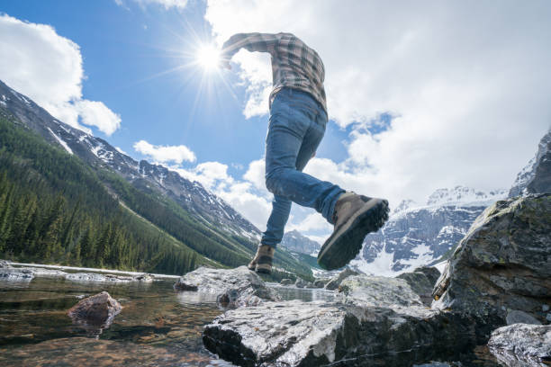 istock Hiker jumps rock to rock on mountain lake 813385564