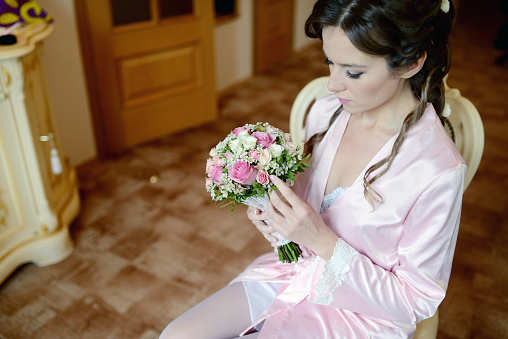 Beauty bride in dressing gown with bouquet and lace veil indoors. Beautiful model girl in colorful wedding robe. Female portrait of cute lady. Woman with hairstyle