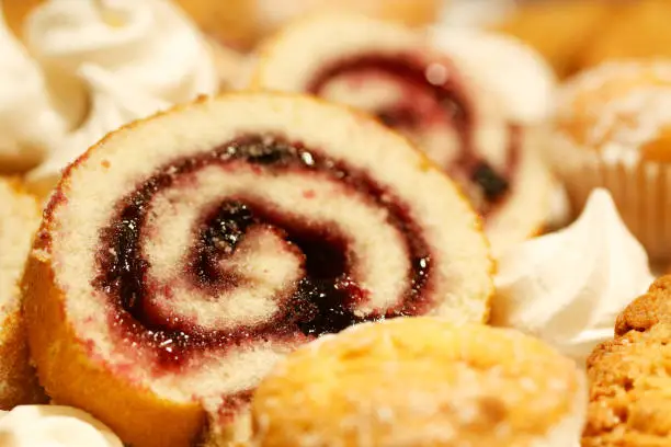 Closeup of swiss roll cake with jam and other sweeties. Selective focus.