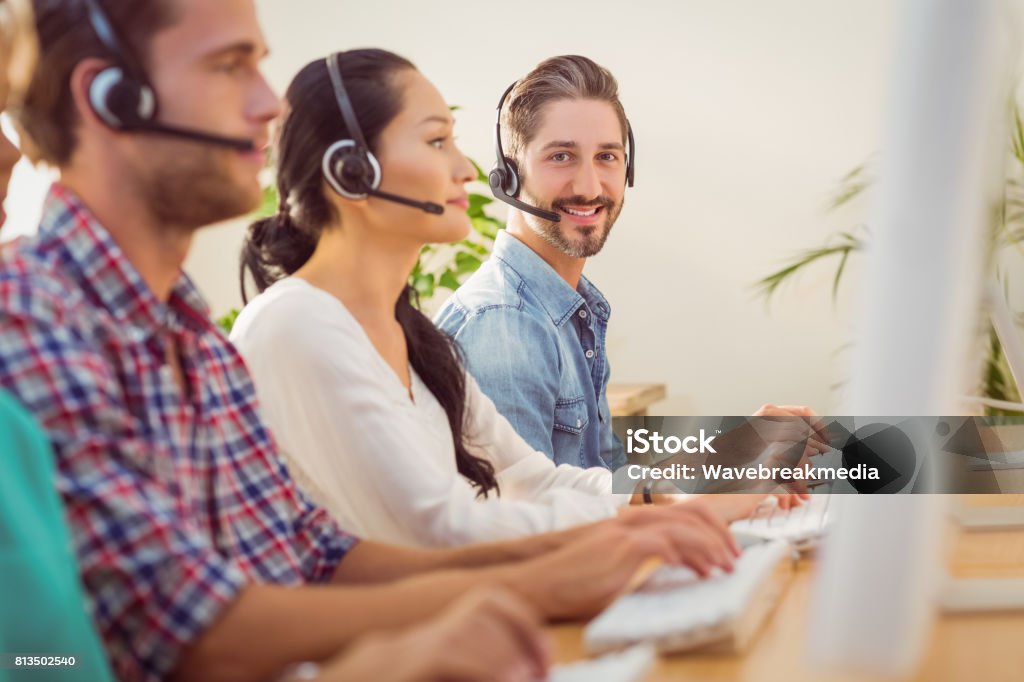 Smiling businessman working in a call centre Portrait of a smiling businessman working with colleagues in a call centre Call Center Stock Photo