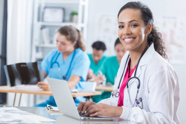 Cheerful medical intern uses a laptop in the classroom Beautiful African American female medical intern uses a laptop during class. She is smiling at the camera. md in usa stock pictures, royalty-free photos & images