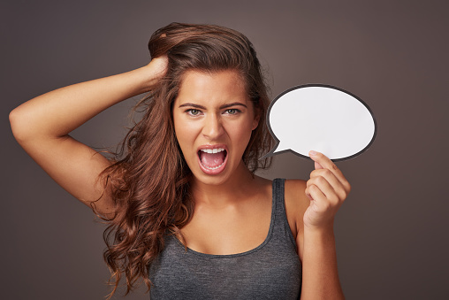 Studio shot of an attractive young woman holding a blank speech bubble and shouting against a gray background