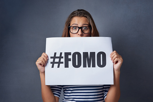 Studio shot of an attractive young woman holding a sign with #FOMO printed on it against a gray background