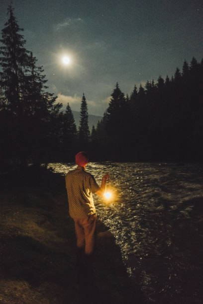 istock Man with gas lantern standing near the river at night 813621662