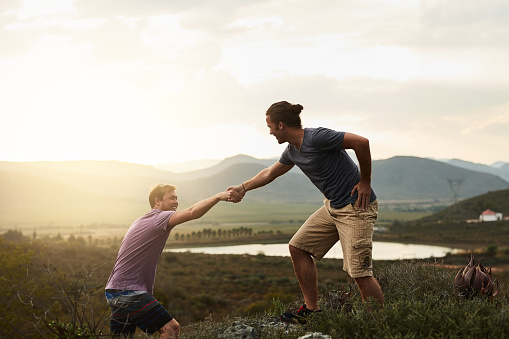 Shot of a friendly young hiker helping his friend climb onto a rock on a mountain trail