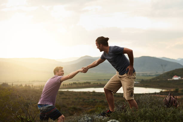 You'll aways find a helping hand on the trail Shot of a friendly young hiker helping his friend climb onto a rock on a mountain trail hand pull up stock pictures, royalty-free photos & images