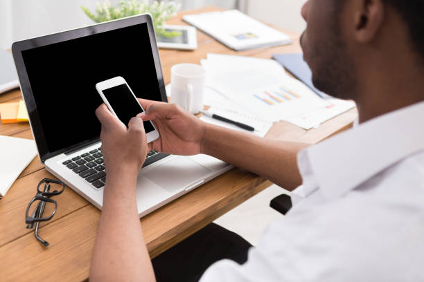 African-american businessman with mobile working at laptop in modern office, crop, closeup, empty screen for copy space