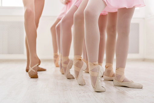 Ballet background, young ballerinas training. Little dancers legs in pointe shoes, making exercises. Classical dance school, copy space